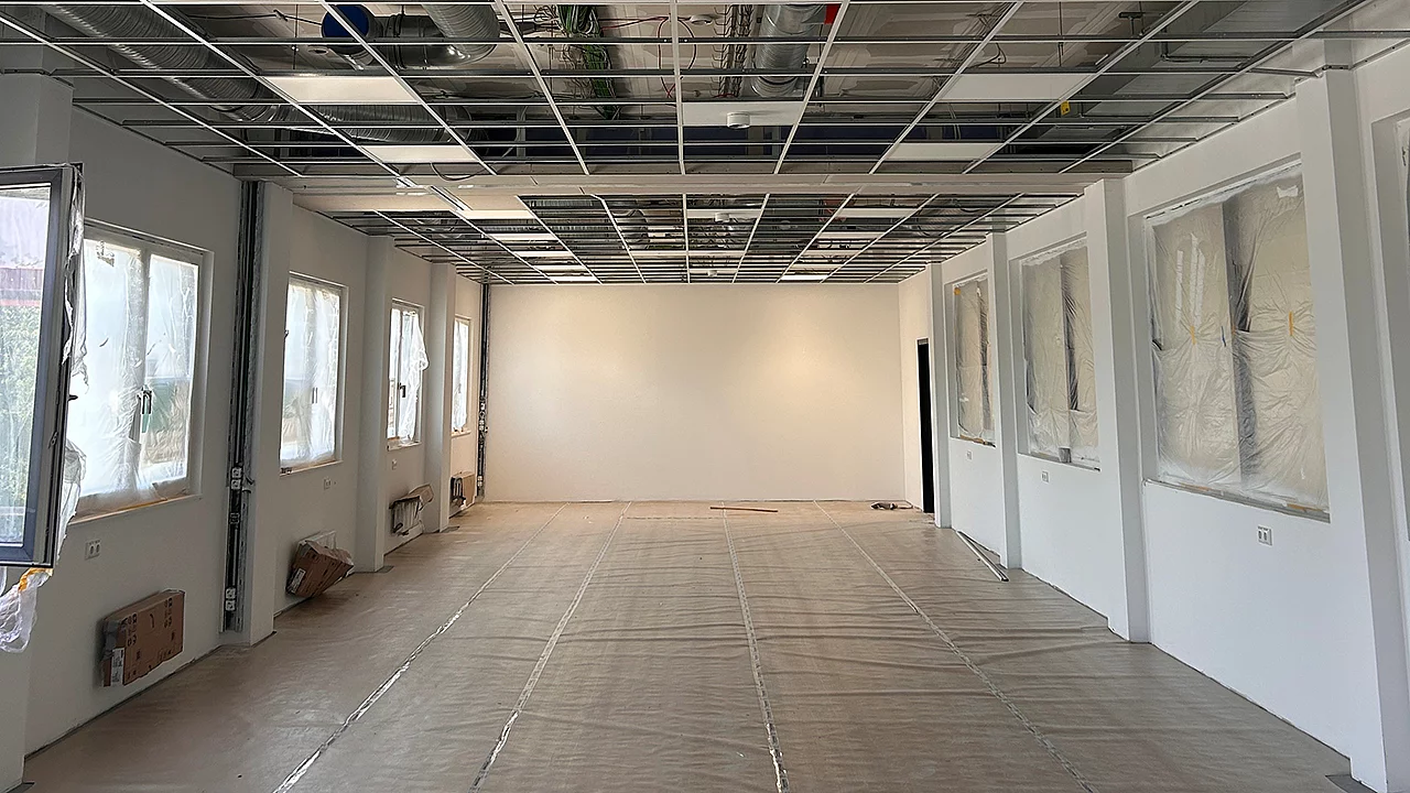Großer Schulraum im Innenausbau mit montierter Unterkonstruktion für die Rasterdecke, vorbereiteten Wänden und geschütztem Boden während der Bauphase