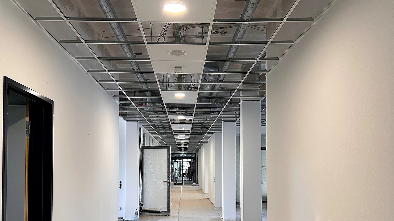 Flur im Ausbau mit teilweise montierter Rasterdecke, integrierter Beleuchtung und sichtbarer Haustechnik vor Fertigstellung.