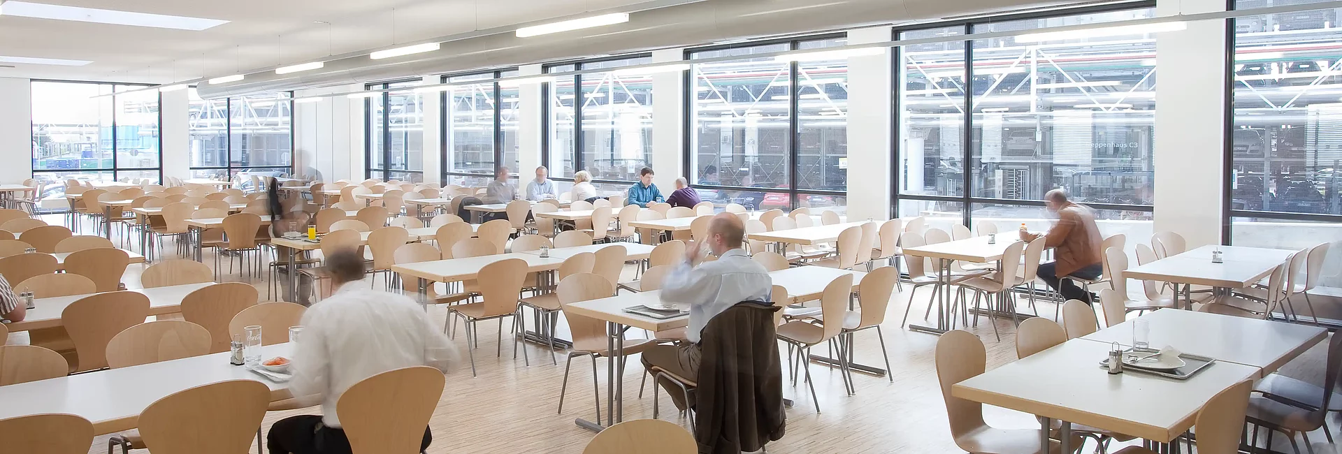 Moderne Betriebskantine mit großzügigem Sitzbereich, hellen Räumen und großen Fensterfronten für Mitarbeitende eines Unternehmens.