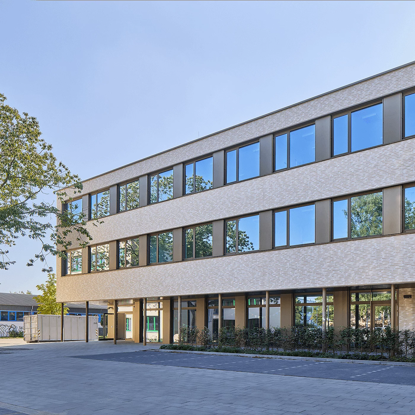 Modernes, dreigeschossiges Büro- und Verwaltungsgebäude mit heller Klinkerfassade, großen Fensterflächen und überdachtem Eingangsbereich an einem sonnigen Tag.