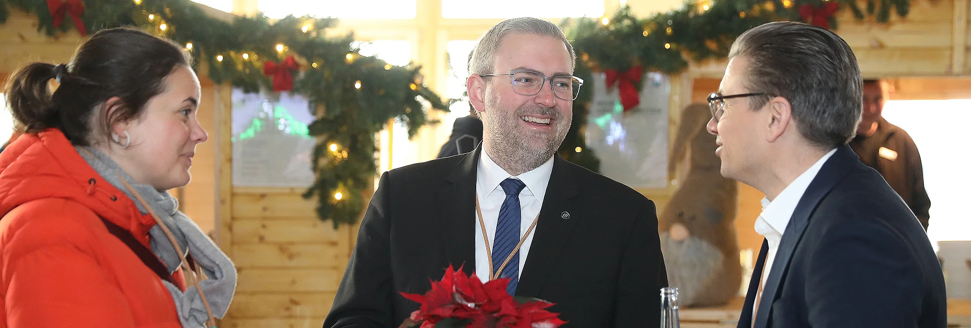 Drei Personen unterhalten sich auf einem weihnachtlich geschmückten Marktstand