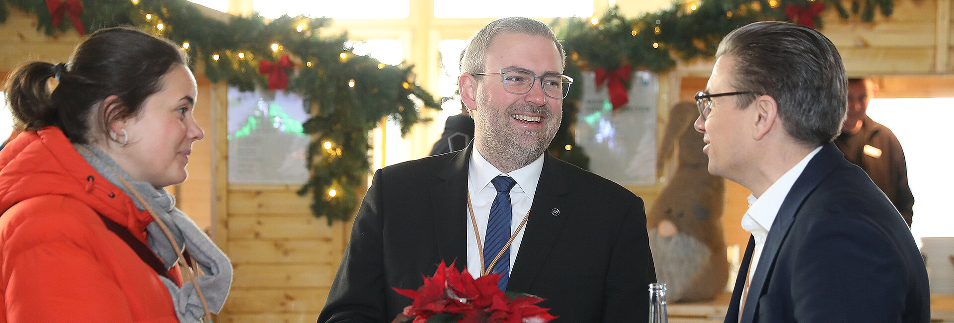 Drei Personen unterhalten sich auf einem weihnachtlich geschmückten Marktstand