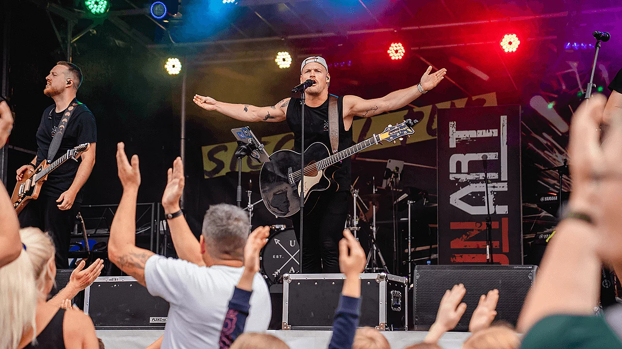 Live-Band auf einer Bühne während eines Konzerts. Zuschauer applaudieren vor der Bühne.