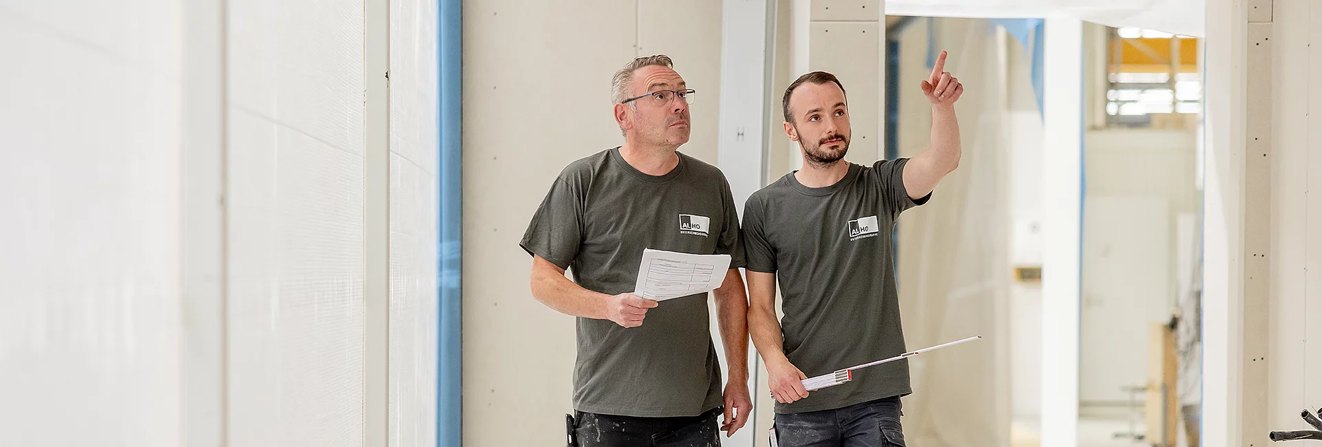 Zwei Mitarbeiter prüfen in einem hellen Innenraum Bauunterlagen und zeigen auf Details