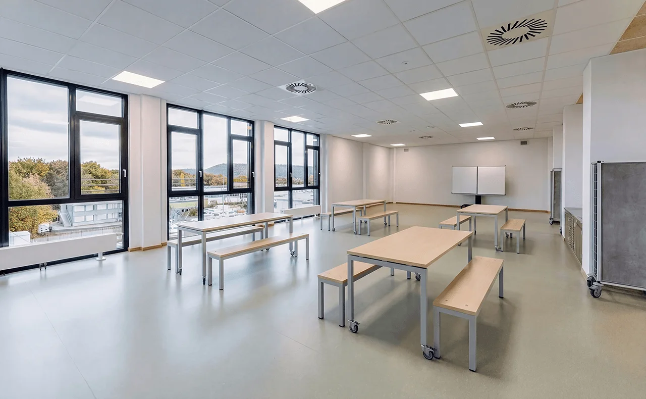 Großer heller Unterrichtsraum mit mobilen Tischen, Bänken, Whiteboard und Fensterfront
