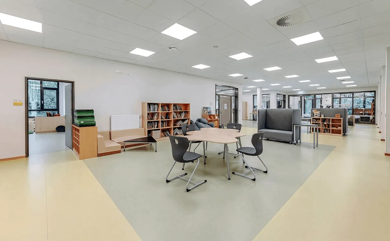 Offener Aufenthaltsbereich mit Tischen, Stühlen, Bücherregalen und Sitzmöbeln