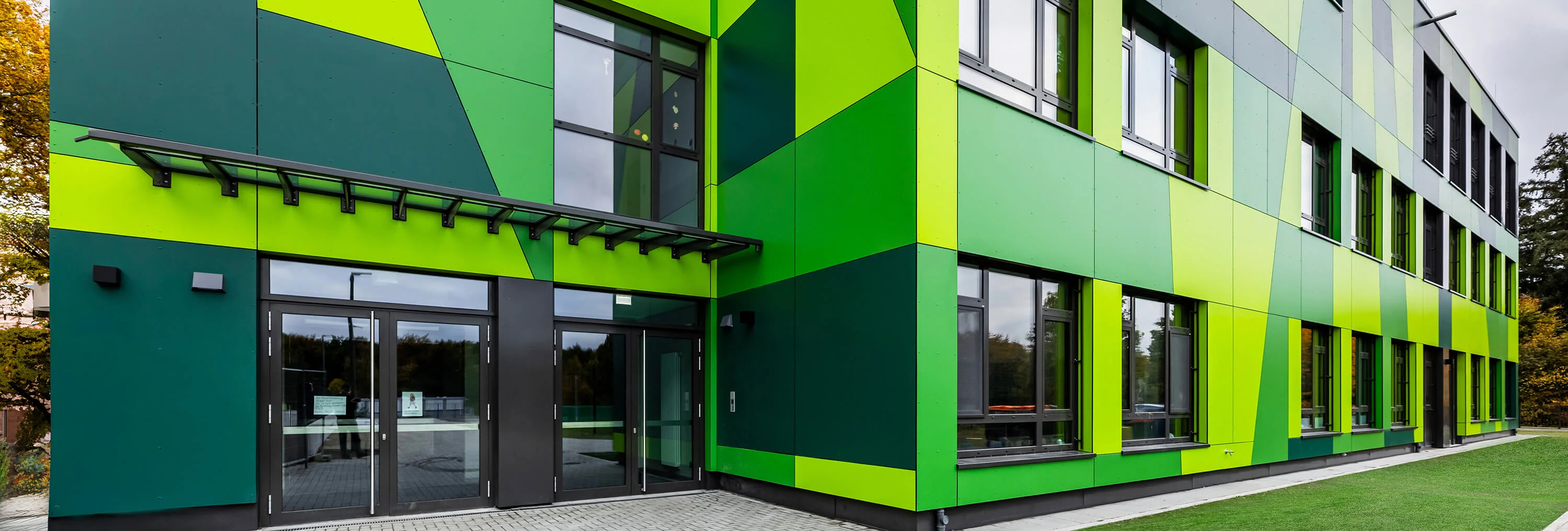 Modernes Gebäude mit grüner Fassadengestaltung, Glas-Eingang und großen Fenstern