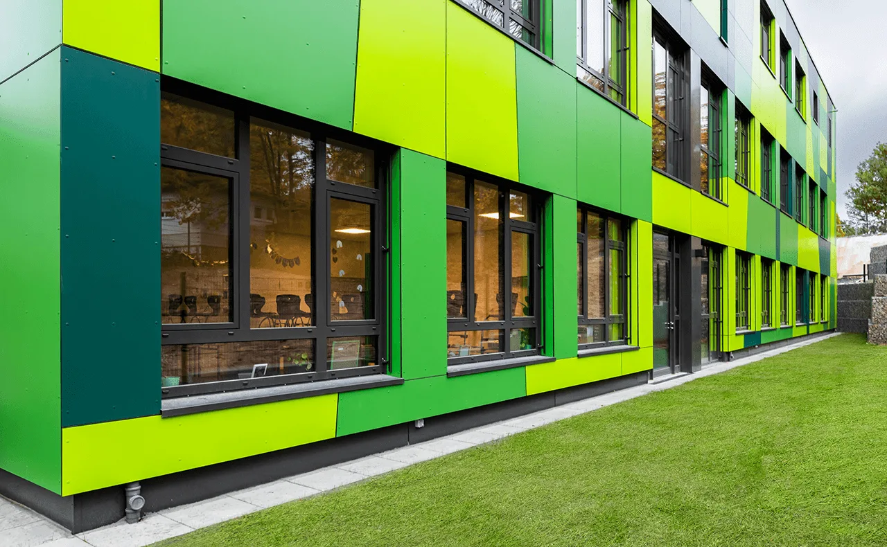 Modernes Gebäude mit grüner Fassadenverkleidung, großen Fenstern und gepflegter Rasenfläche