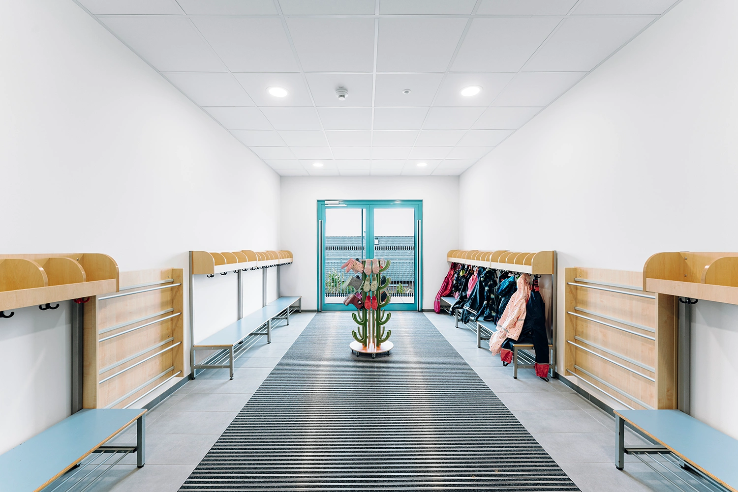 Helle Garderobe mit Sitzbänken, Kleiderhaken, Jacken und Schuhbaum in einem modernen Gebäude