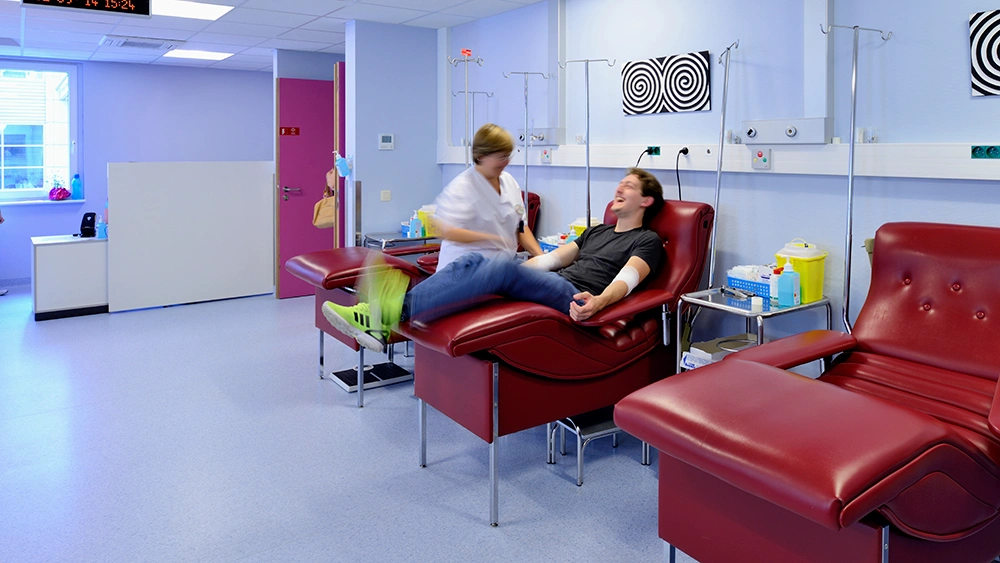 Patient in einem Behandlungsstuhl wird von einer Pflegekraft in einem modernen medizinischen Behandlungsraum betreut