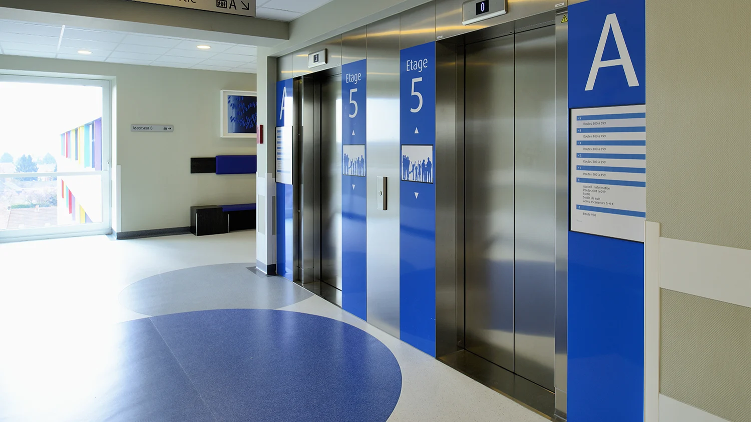 Aufzugsbereich in einem Klinikgebäude mit blauen Etagenmarkierungen und hellem Flur