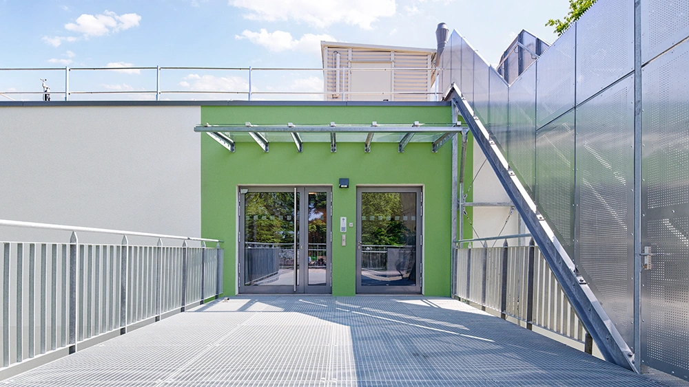 Dachterrasse mit Metallsteg, grünem Eingangsbereich und technischer Gebäudeausstattung
