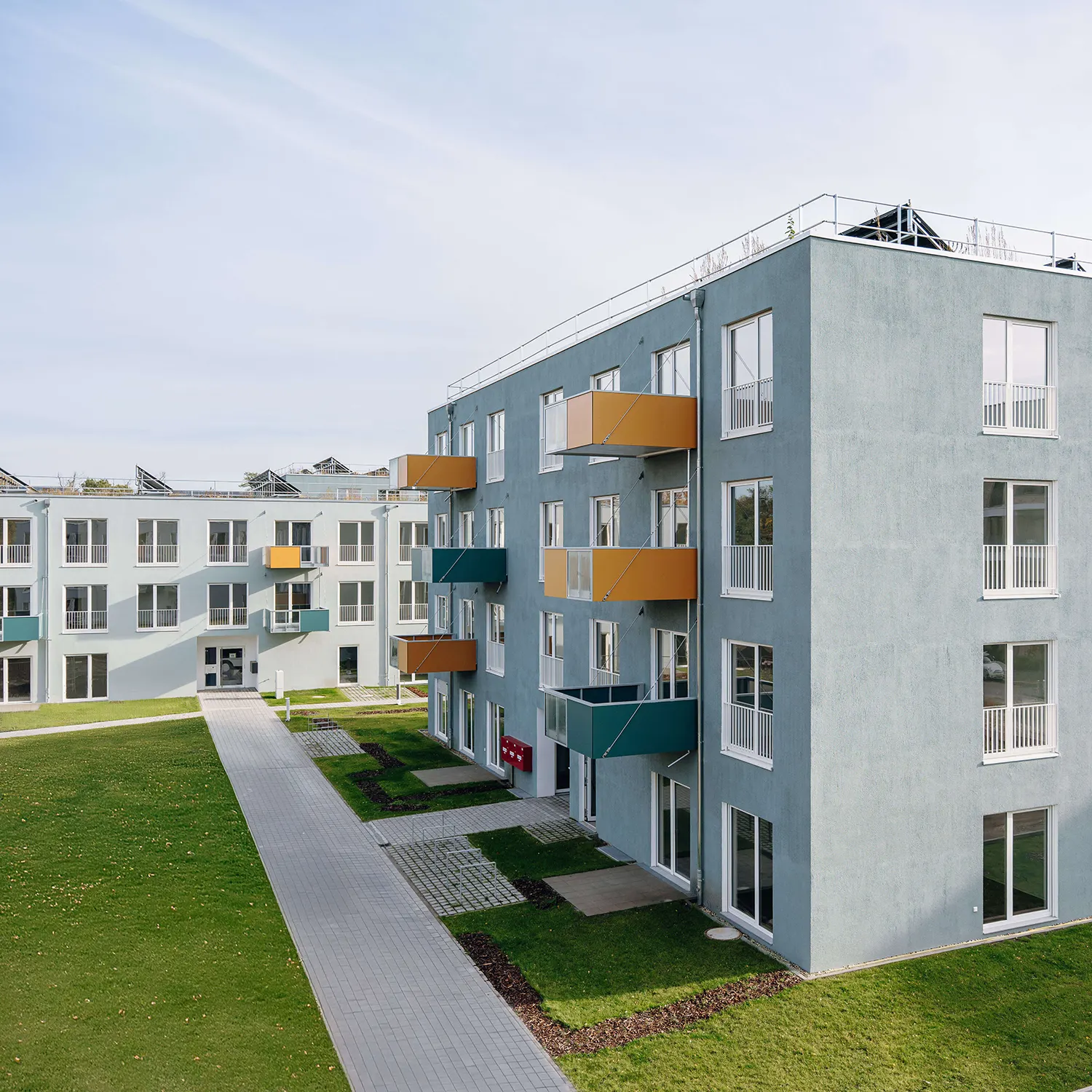 Modernes Wohngebäude mit grauer Fassade, farbigen Balkonen und begrüntem Außenbereich