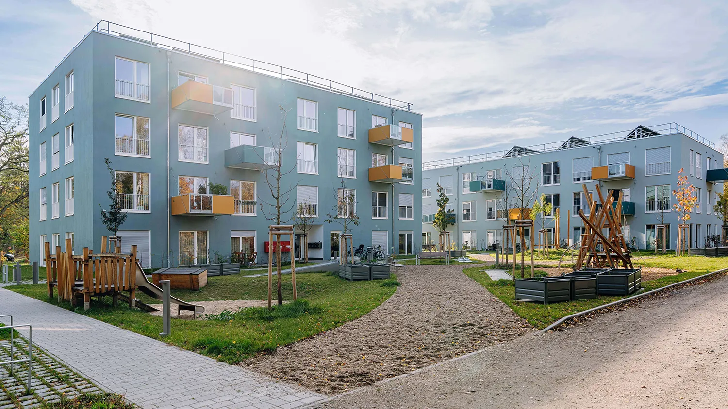 Moderne Wohngebäude mit farbigen Balkonen, Spielplatz, Grünflächen und Wegen im Innenhof