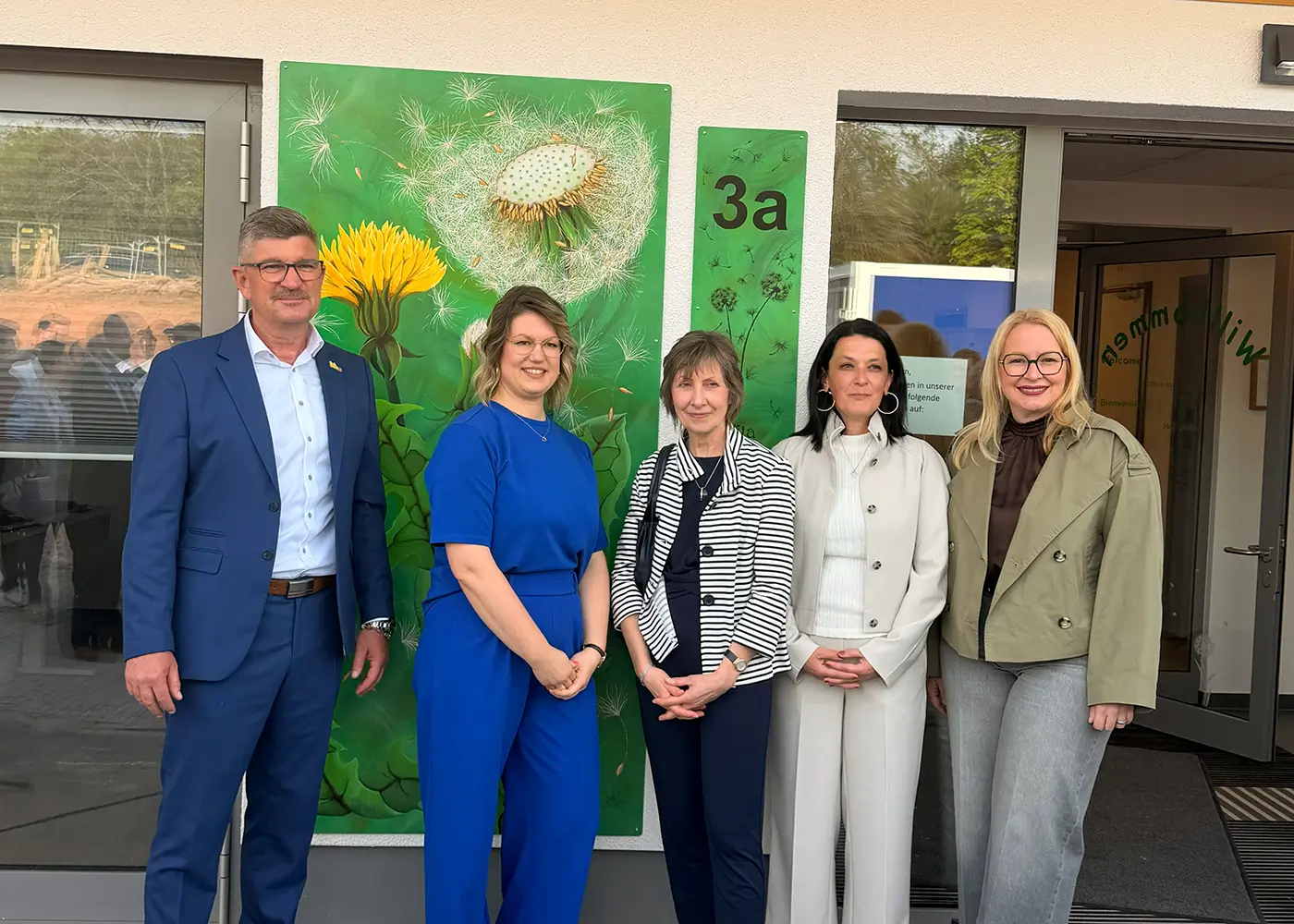 Fünf Personen stehen vor dem Eingang eines Gebäudes mit grüner Wandgestaltung.