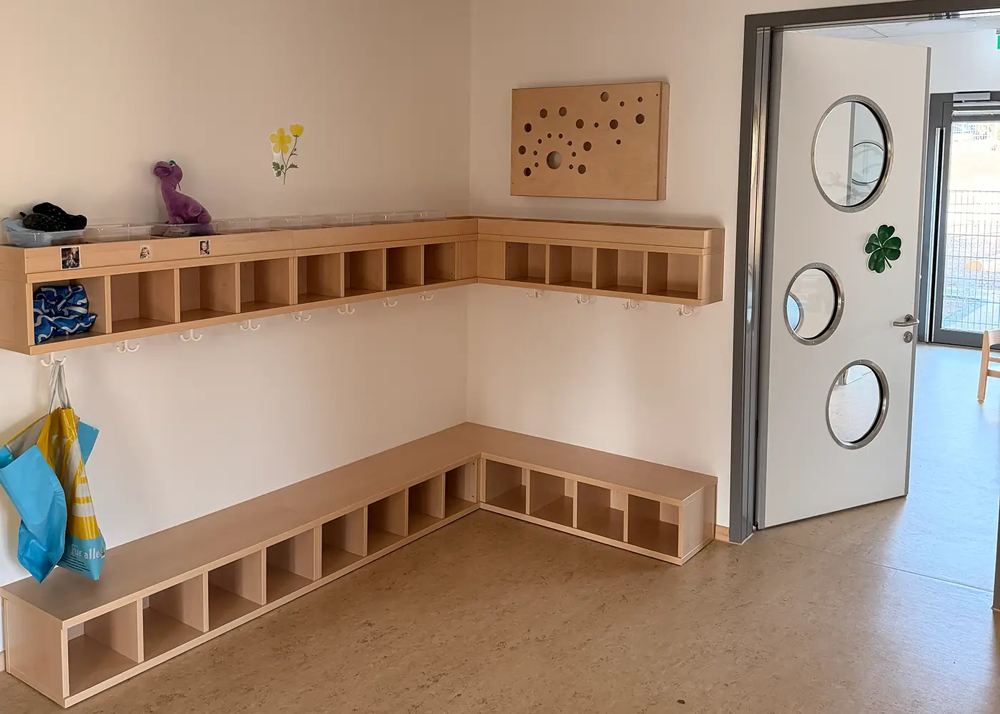 Heller Garderobenbereich mit Holzbänken, Fächern und Haken für Kinder.