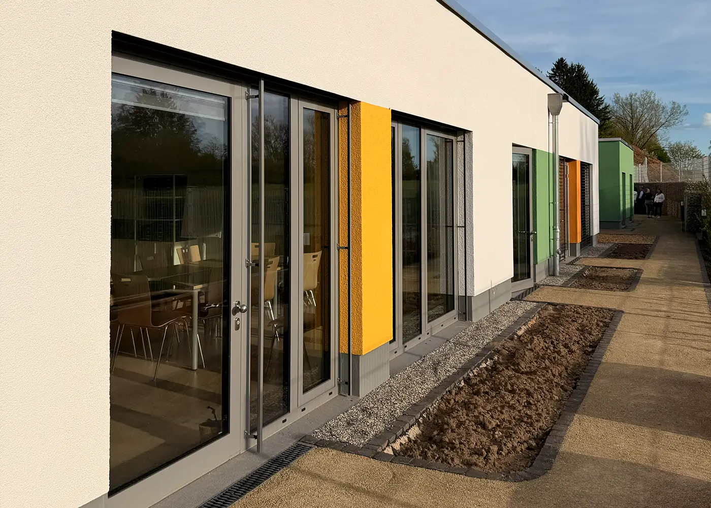 Moderne Gebäudefassade mit großen Fenstern und farbigen Akzenten.
