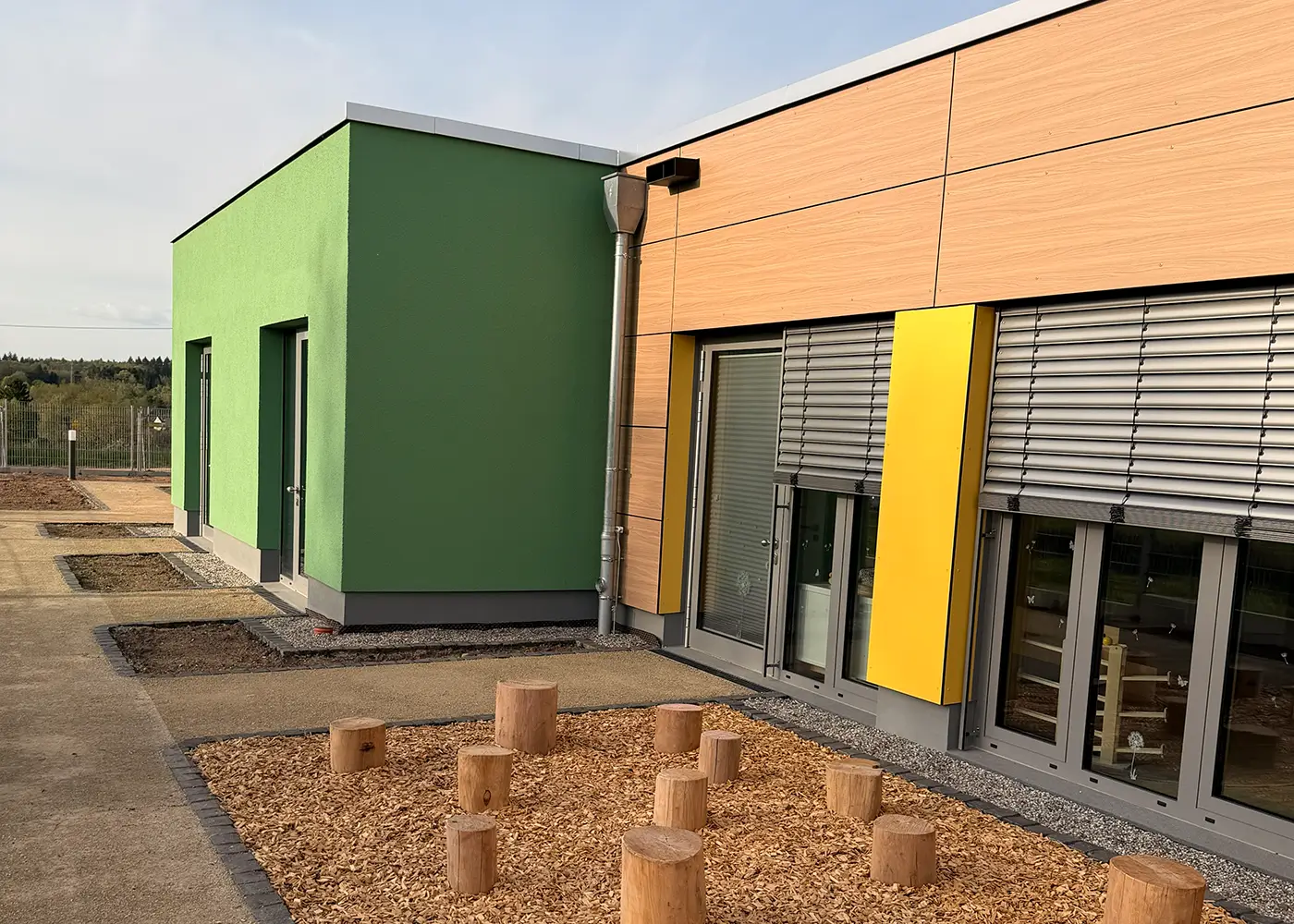 Außenbereich mit Holz-Elementen vor einem farbigen Neubau.