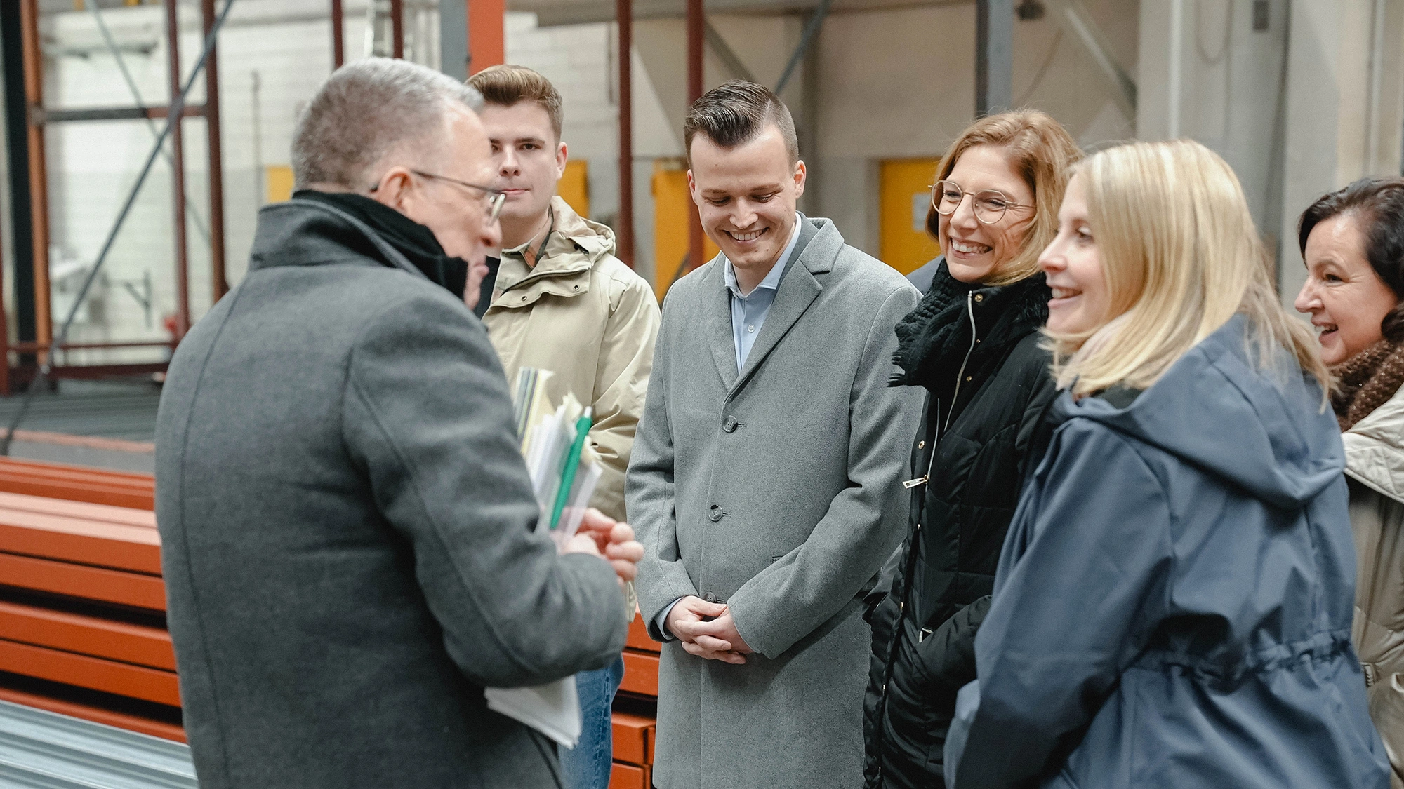 Besuchergruppe erhält in einer Produktionshalle eine Führung zwischen gestapelten Bauelementen