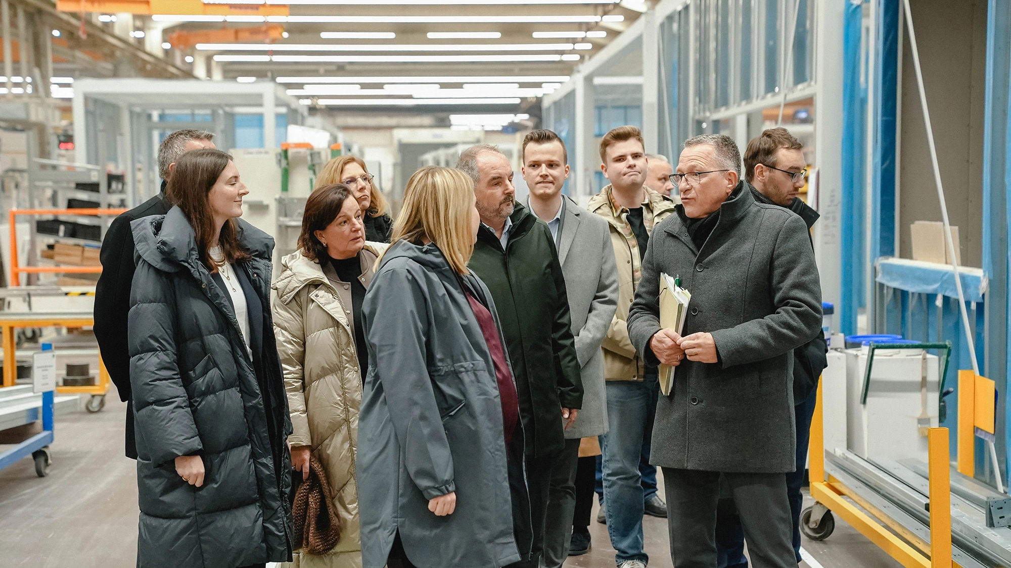 Besuchergruppe erhält eine Führung durch eine Produktionshalle mit Bauelementen und Fenstern