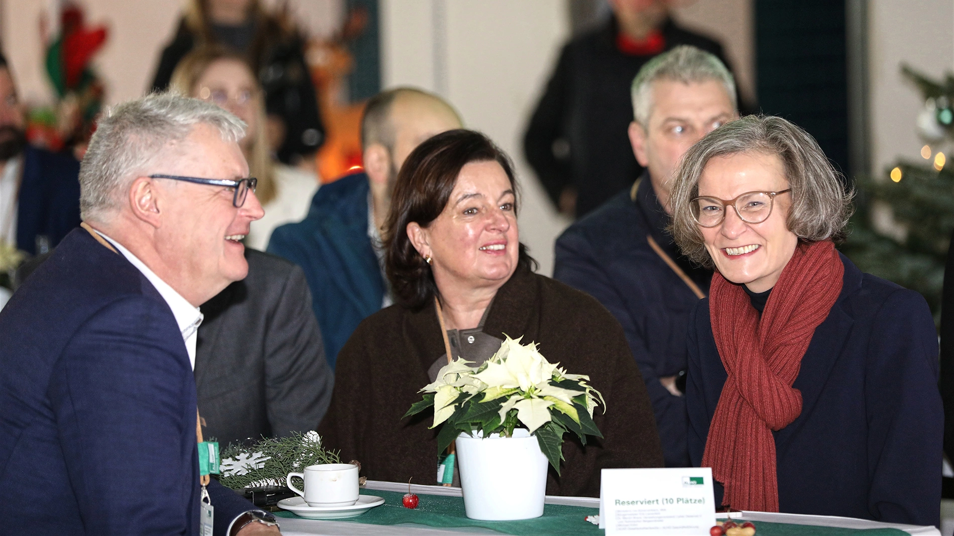 Drei Personen sitzen bei einer Veranstaltung an einem Tisch mit Weihnachtsdekoration und unterhalten sich
