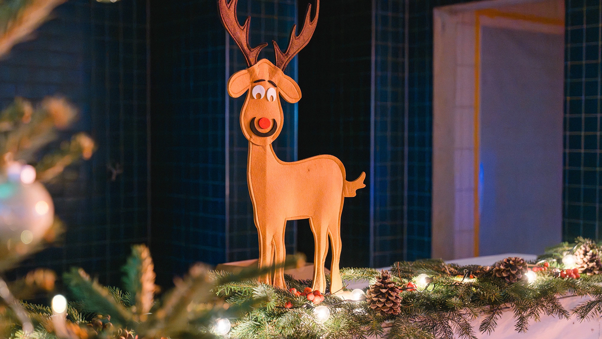 Weihnachtliche Dekoration mit beleuchtetem Rentier, Tannengrün, Zapfen und Lichterkette