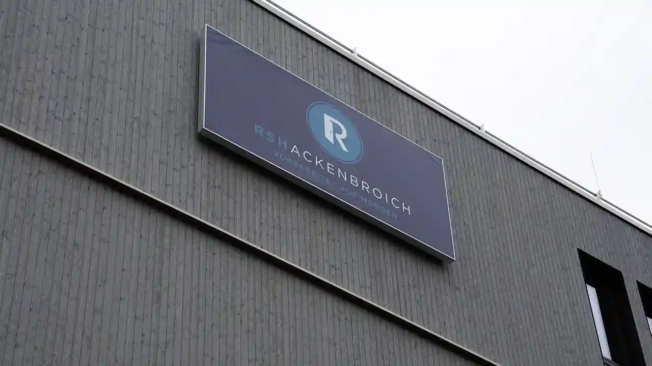 Außenansicht einer modernen Gebäudefassade mit großem Firmenschild „RSHACKENBROICH – Vordenker für morgen“ an einer dunkel verkleideten Wand.